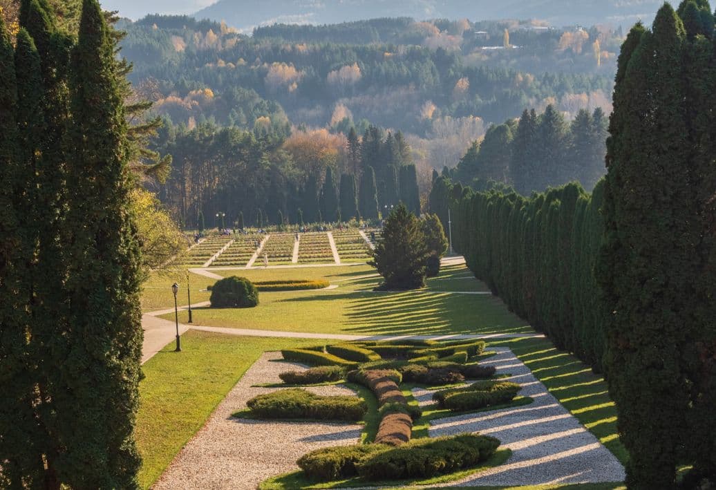 Живописный парк с ухоженными кустарниками и кипарисами на фоне горного пейзажа.